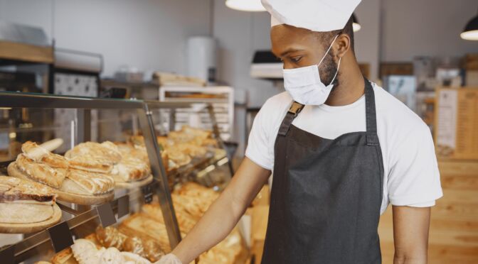 NetSuite Food and Beveragebaker-uniform-giving-advice-about-pastry-man-wearing-protective-mask-buying-fresh-bread-min