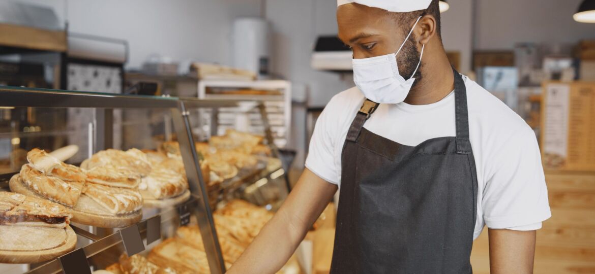 NetSuite Food and Beveragebaker-uniform-giving-advice-about-pastry-man-wearing-protective-mask-buying-fresh-bread-min